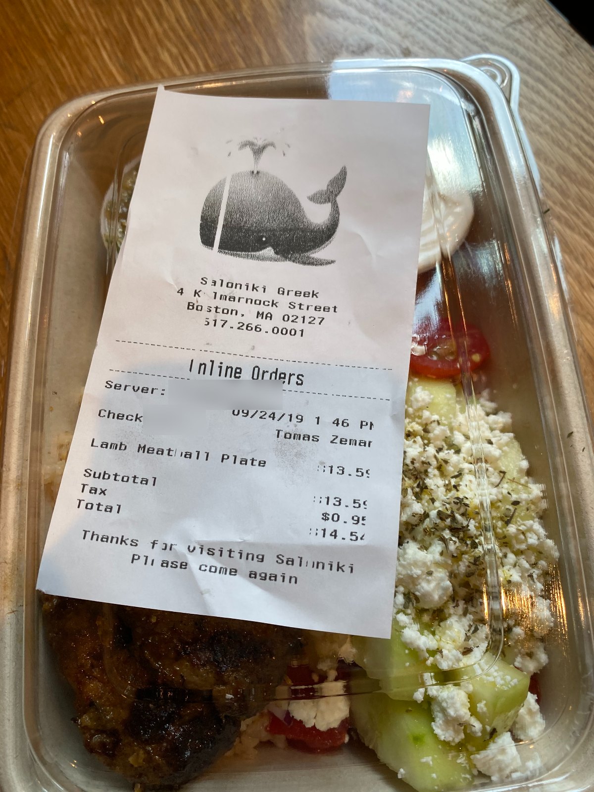 Un ticket de commande à emporter de Saloniki Greek à Boston, daté du 24/09/19, avec une grande baleine imprimée en haut, posé sur une assiette de boulettes d'agneau
