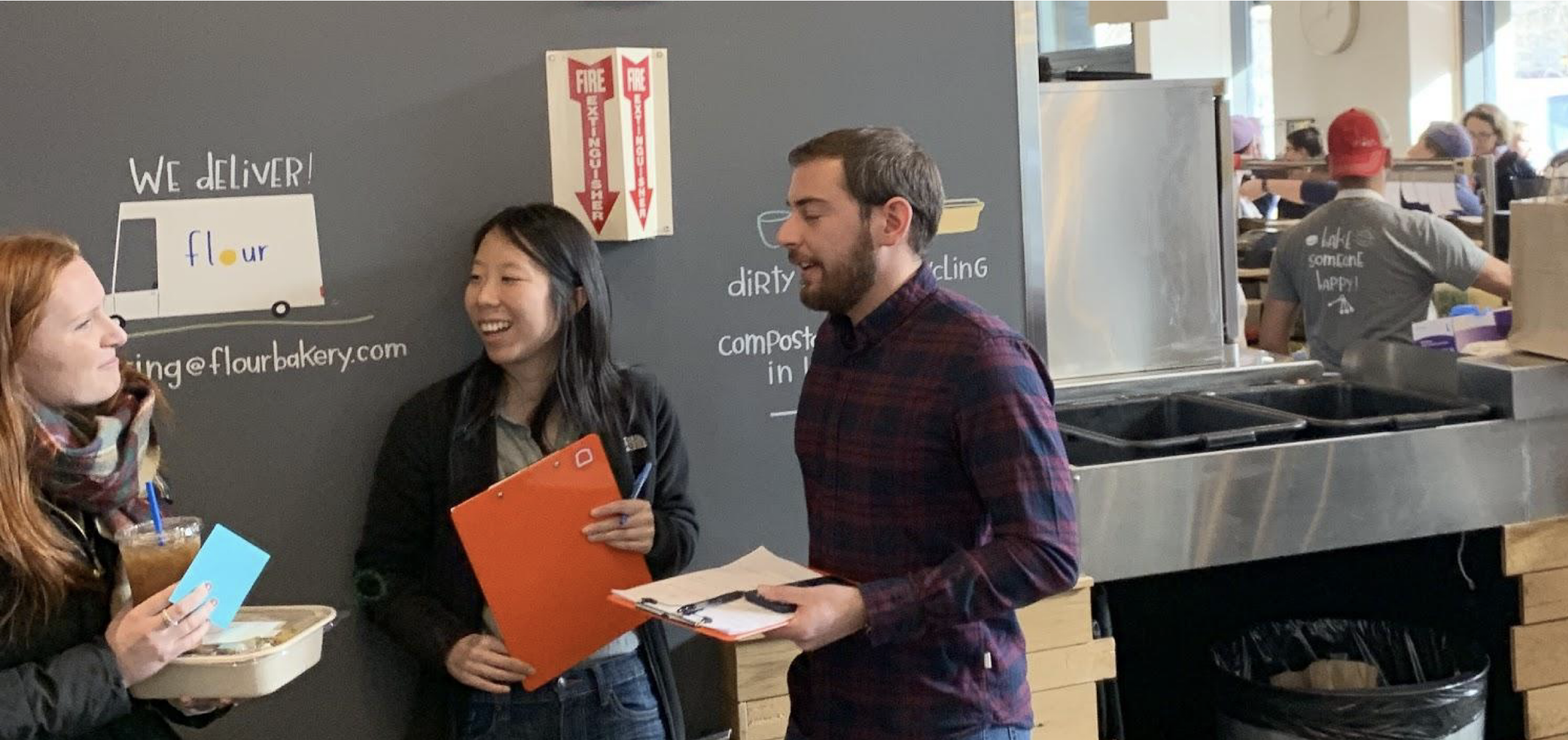 The team interviewing a restaurant operator with clipboards in a working cafe